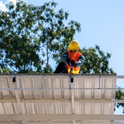 Roofer worker in protective uniform wear and gloves working installing metal sheet on top of the new roof at construction site.